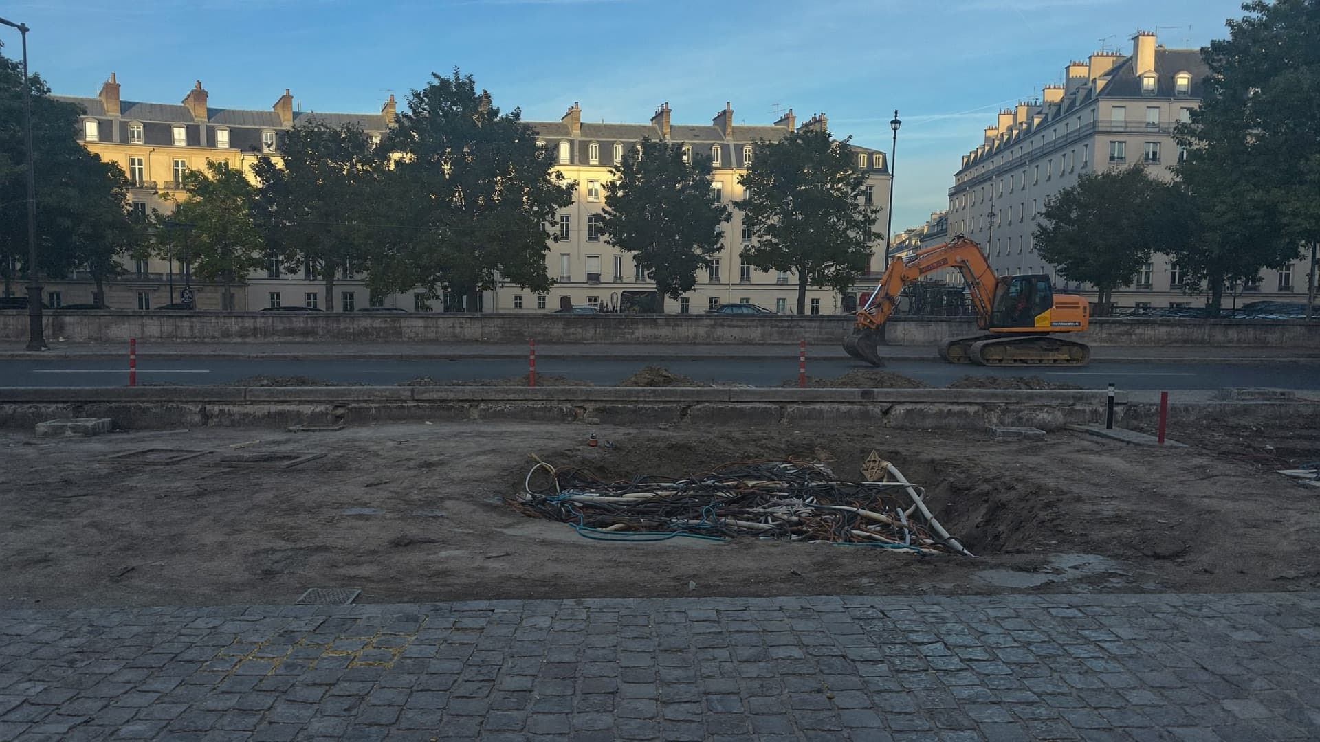 Une tranchée ouverte le long d'un quai parisien, câbles à nu, une pelle mécanique en arrière-plan